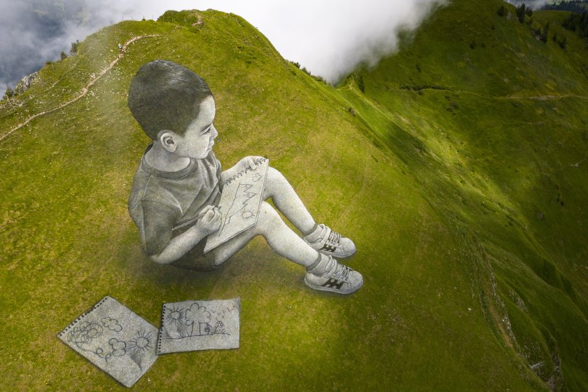 Художник изрисува две гигантски биоразградими лендарт картини върху зелените треви